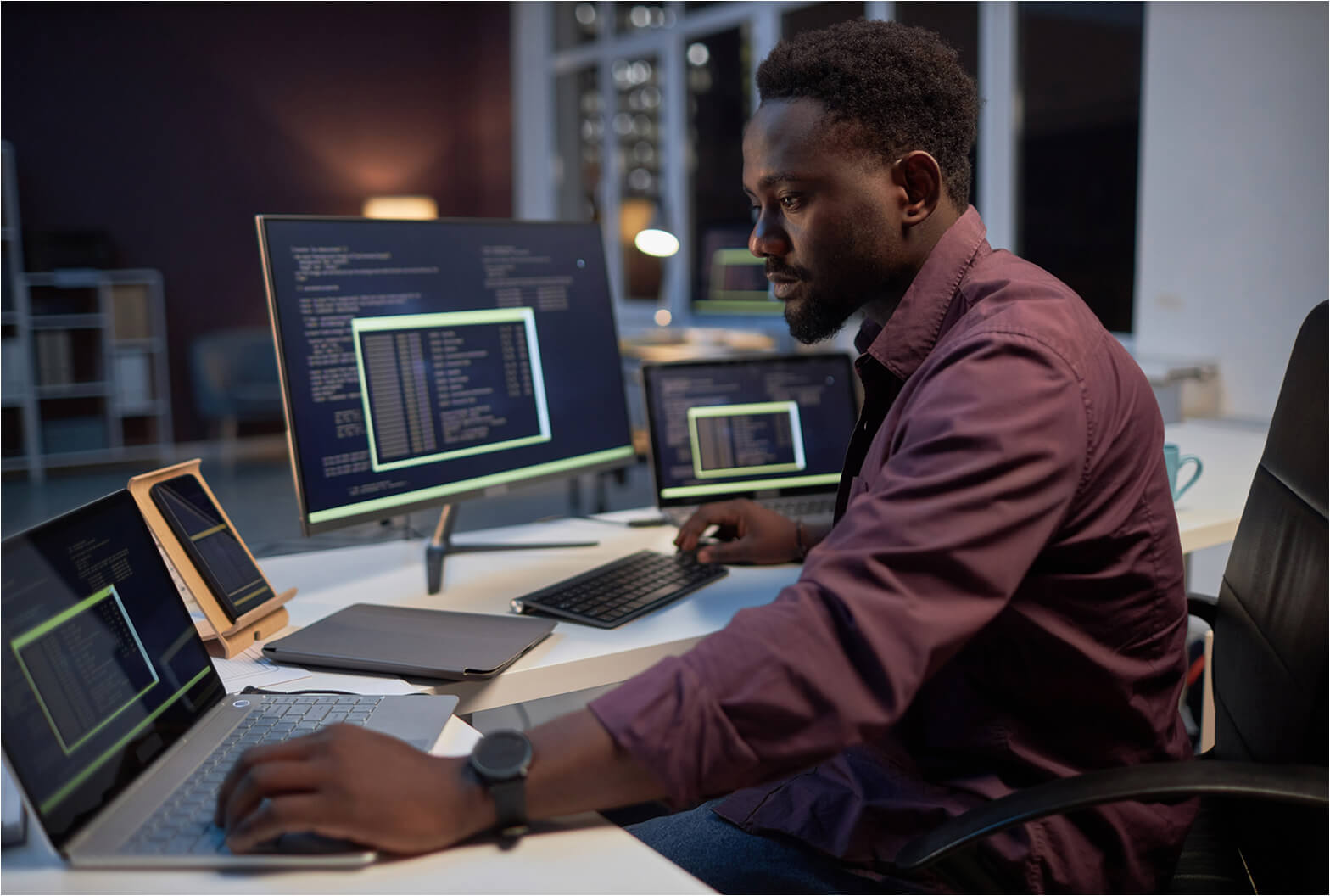 A professional reviewing compliance data across multiple screens displaying code in a modern office at night.