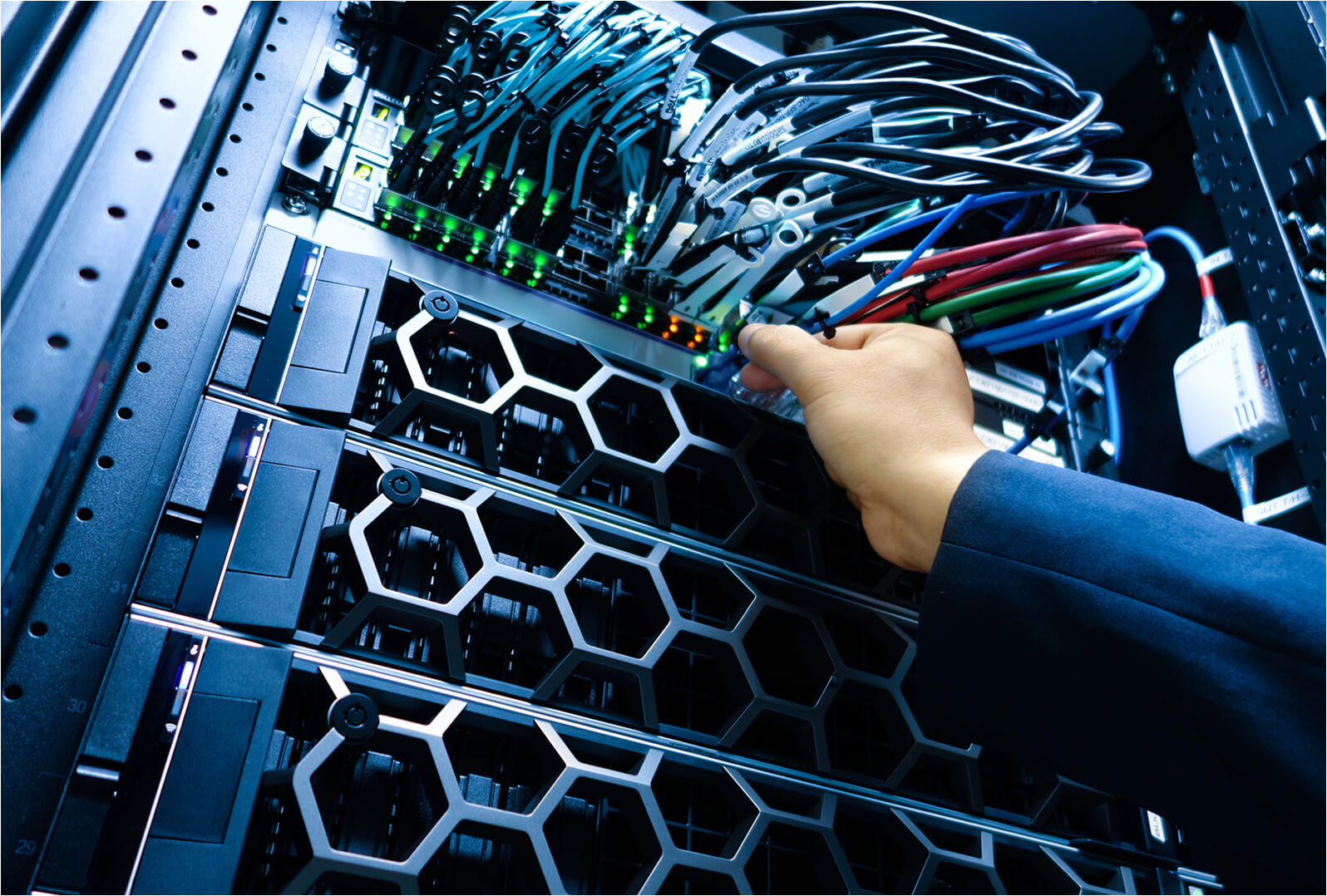 A technician's hand adjusts cables on a rack-mounted server with honeycomb ventilation panels and green indicator lights.