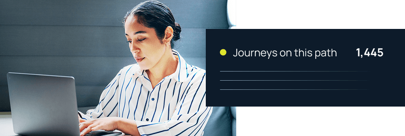 A professional woman in a striped shirt works on a laptop beside a dashboard displaying 1,445 journeys on a path.