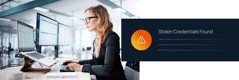 A woman working at a desk with multiple monitors beside a "Stolen Credentials Found" warning alert notification.