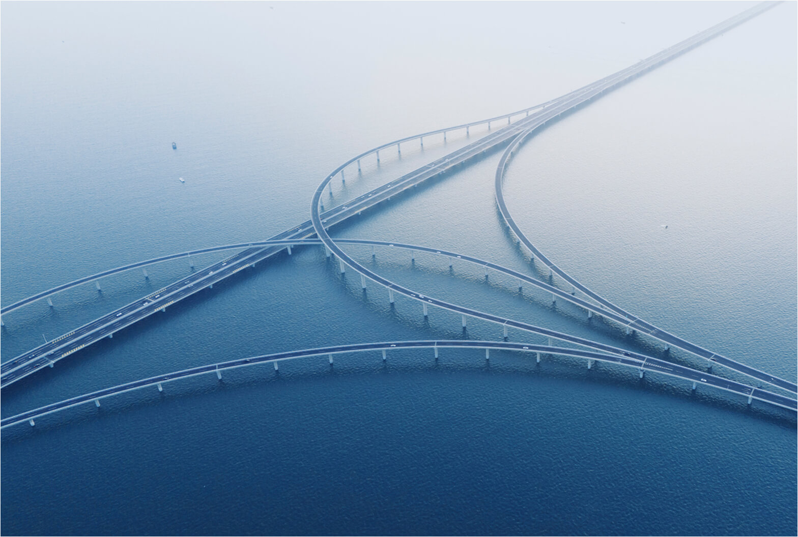 Aerial view of sweeping highway bridges curving and intersecting over a vast, calm blue ocean.