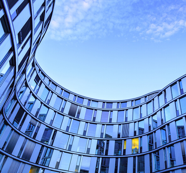 Modern curved glass office building with sweeping architectural lines against a blue sky, representing diverse industries.