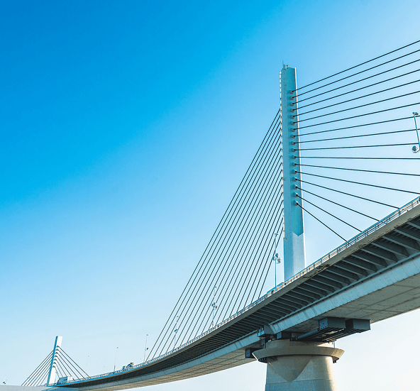 Modern cable-stayed bridge with tall white pylons and steel cables against a clear blue sky, representing critical