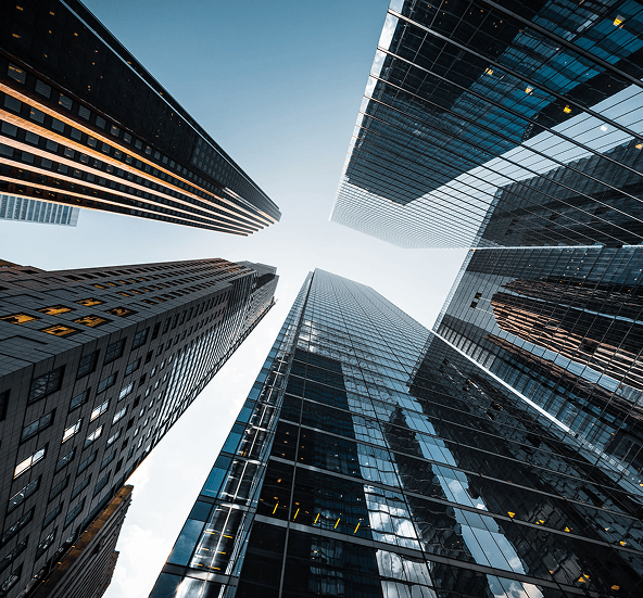 Upward view of modern glass skyscrapers in a financial district converging against a clear blue sky.